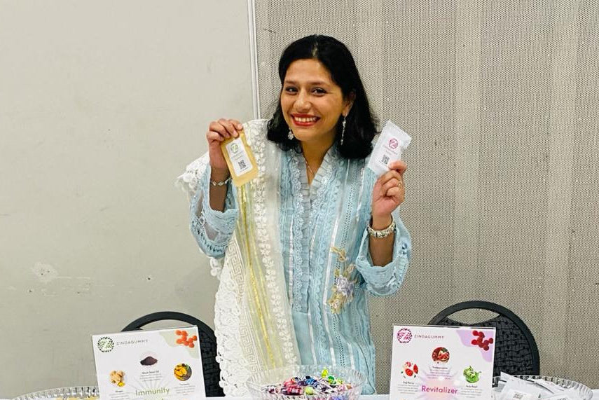 Woman holding two products in front of a table with promotional materials and snacks.